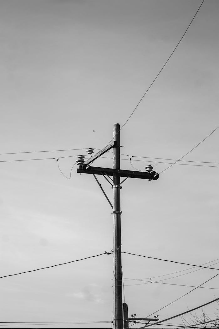 Black and white photo of a utility pole with power lines stretching across an empty sky.